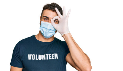 Hispanic young man wearing medical mask and volunteer t shirt smiling happy doing ok sign with hand...