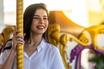 The asian young woman happily smiling and sitting in the carousel of the amusement park