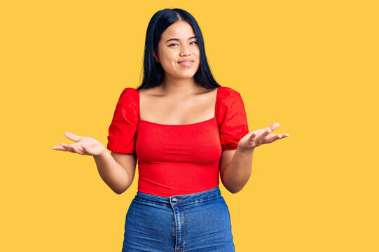 Young beautiful asian girl wearing casual clothes clueless and confused expression with arms and hands raised. doubt concept.