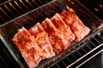 raw pork ribs sprinkle with salt, black pepper and paprika in a glass baking tray in the oven. cooking meat at home. Cook.