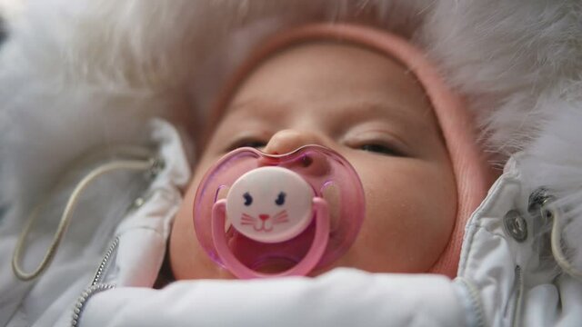 Cute baby sucks pacifier in mother's hands. Close-up.