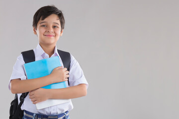 portrait of a school boy smiling with bag and books in hand 	