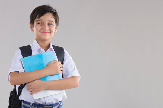 portrait of a school boy smiling with bag and books in hand 	