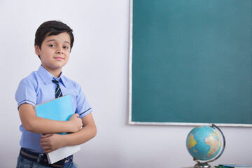 school boy standing in front of blackboard with a book	