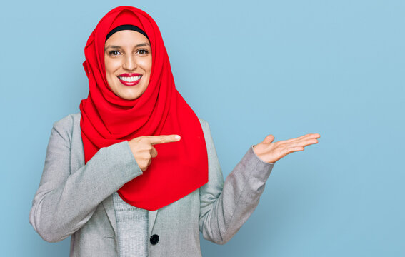 Beautiful hispanic woman wearing traditional islamic hijab scarf amazed and smiling to the camera while presenting with hand and pointing with finger.