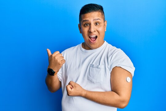 Young latin man using glucose meter button pointing thumb up to the side smiling happy with open mouth