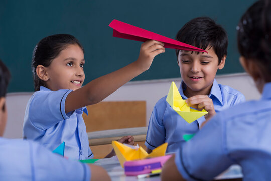 children playing with paper plane and boat in class	