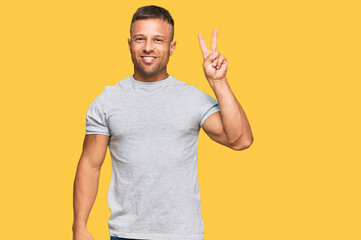 Handsome muscle man wearing casual grey tshirt smiling with happy face winking at the camera doing victory sign. number two.