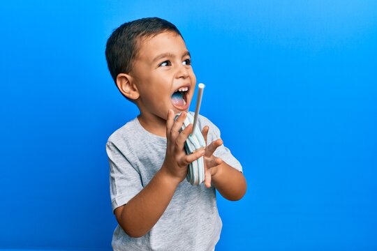 Adorable latin toddler eating delicious lollipop over isolated blue background.