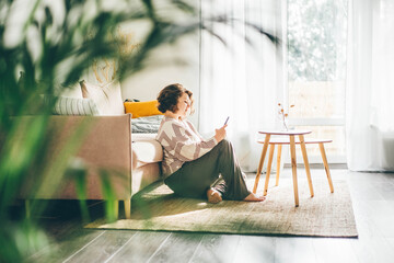 Smiling woman looking at cell phone at sunny home.