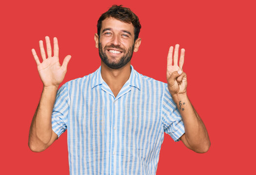 Handsome young man with beard wearing casual fresh shirt showing and pointing up with fingers number eight while smiling confident and happy.