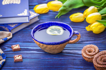 Ceramic cup of lemon tea, spring yellow tulips and books and chocolate pieces with an Easter bunny