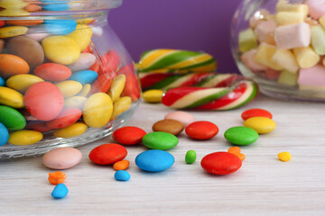 Multi-colored candies in glass jars on a white table. Close-up. Lilac background - 411199894