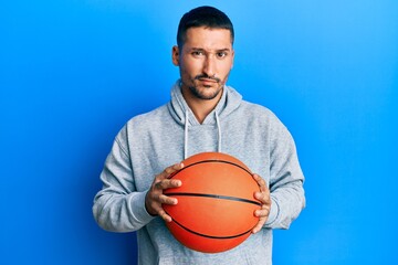 Handsome man with tattoos holding basketball ball skeptic and nervous, frowning upset because of problem. negative person.