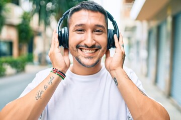 Young hispanic man smiling happy listening to music using headphones at street of city.