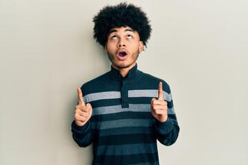 Young african american man with afro hair wearing casual clothes amazed and surprised looking up and pointing with fingers and raised arms.