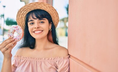 Young hispanic tourist girl wearing summer style holding donut at the city.