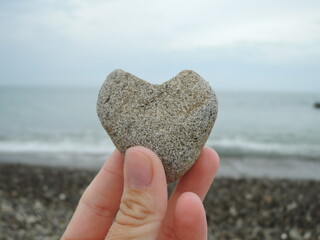Heart shaped stone held in hands, sea in background