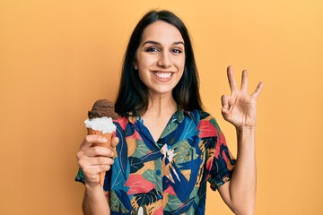 Young hispanic woman holding ice cream doing ok sign with fingers, smiling friendly gesturing excellent symbol