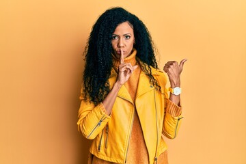 Middle age african american woman wearing wool winter sweater and leather jacket asking to be quiet with finger on lips pointing with hand to the side. silence and secret concept.