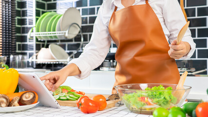 Happy asian women cooking healthy food while looking recipe on digital tablet in the loft kitchen browsing internet website on tutor cooking class, Healthy food and Dieting concept