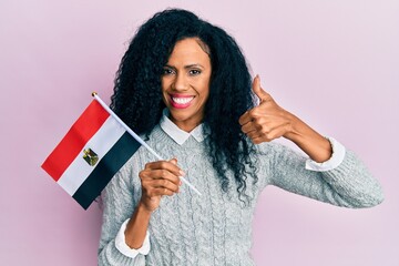 Middle age african american woman holding egypt flag smiling happy and positive, thumb up doing excellent and approval sign