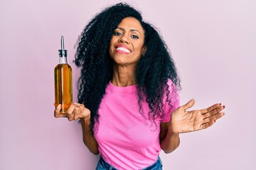 Middle age african american woman holding olive oil can celebrating achievement with happy smile...