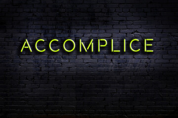 Neon sign. Word accomplice against brick wall. Night view