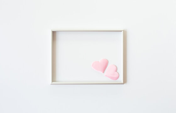 The silver photo frame and two pink hearts are 
in the corner are on a white background. Valentine's day or wedding theme. Free space for text.