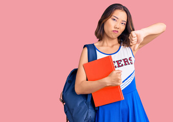 Young beautiful chinese girl wearing cheerleader uniform and student backpack holding binder with angry face, negative sign showing dislike with thumbs down, rejection concept