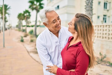 Middle age hispanic couple smiling happy and hugging walking at street.