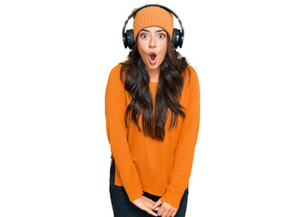 Beautiful brunette young woman listening to music using headphones afraid and shocked with surprise expression, fear and excited face.