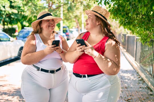 Two plus size overweight sisters twins women with smartphone outdoors on a sunny day