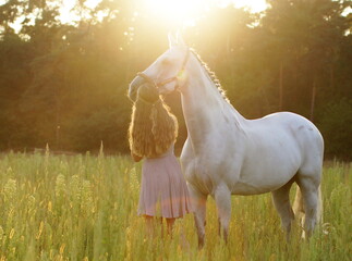 young woman with pink dress and white horse on meadow during sunset - friendship