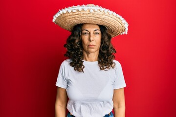Middle age hispanic woman holding mexican hat with serious expression on face. simple and natural looking at the camera.