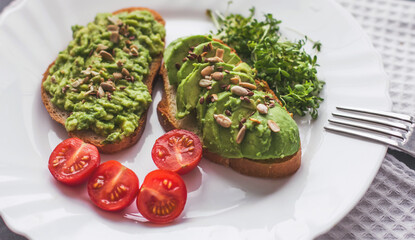 Vegan avocado sandwich with tomatoes and microgreens on a white plate on a gray background