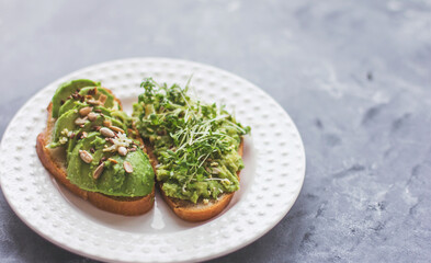 Vegan avocado sandwich with microgreens on a white plate on a gray background