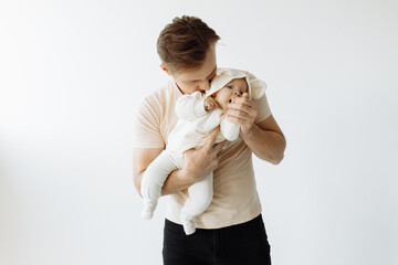 Happy young dad is photographed with his little daughter in the studio on a white background. A caring dad holds the baby in his arms, looks at her. Family and paternity concept.