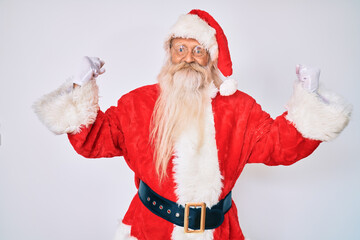 Old senior man with grey hair and long beard wearing santa claus costume screaming proud, celebrating victory and success very excited with raised arms