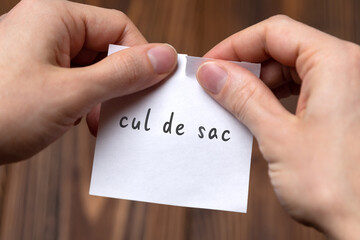 Hands of a man tearing a piece of paper with inscription cul de sac