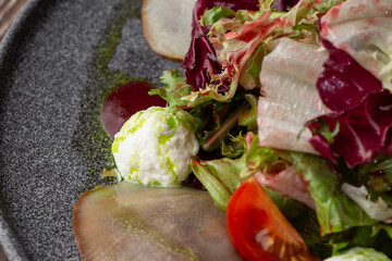 A tasty salad with pear, tomato, mozzarella cheese and fresh lettuce, dressed with a red and green sauces. Macro close-up on a grey round plate on a wooden background. Healthy food.