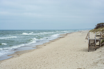 a wide sandy beach and a beautiful dark blue Baltic sea with waves on a cloudy day against the...
