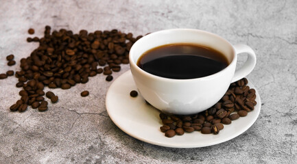 Side view of a cup of coffee surrounded with coffee beans against concrete background.