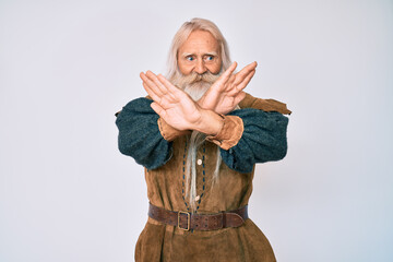 Obraz premium Old senior man with grey hair and long beard wearing viking traditional costume rejection expression crossing arms and palms doing negative sign, angry face