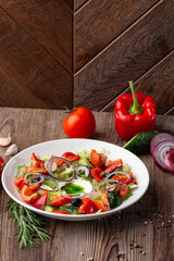 Greek salad with fresh vegetables: tomato, cucumber, red bel pepper, lettuce, onion, olives and cheese. Close-up on a white round plate on a wooden background. Salad menu with ingredients.