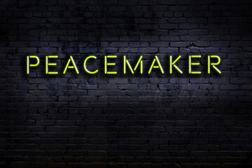 Neon sign. Word peacemaker against brick wall. Night view