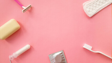 women's personal care items on a pink background. a condom,a tampon, a toothbrush, soap, towel.