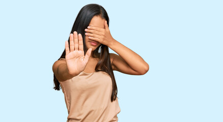 Beautiful hispanic woman wearing casual clothes covering eyes with hands and doing stop gesture...