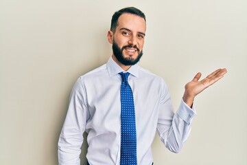 Young man with beard wearing business tie smiling cheerful presenting and pointing with palm of hand looking at the camera.