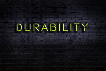 Night view of neon sign on brick wall with inscription durability